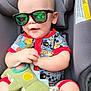 baby, child, sunglasses, car_seat, plush_toy, dinosaur_toy, smiling, infant, cute, clothing, seat_belt, red_trim, happy, indoors, person, toy, hand, legs, head, face