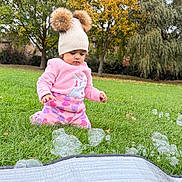 Diara joined the competition — help win amazing prizes! toddler, child, pink_clothing, hat, pom_poms, bubbles, grass, outdoor, autumn, trees, greenery, cute, curious, playful, nature, fall, park, young_child, sitting, daylight
