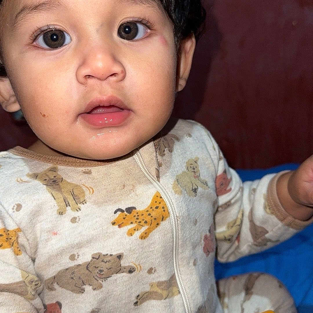 Dominic joined the competition — help win amazing prizes! baby, child, portrait, close_up, wide_eyed, looking_at_camera, indoor, seated, onesie, pajamas, animal_print, cat_pattern, toy, colorful_toy, playtime, dark_hair, brown_eyes, red_background, text_overlay, infant