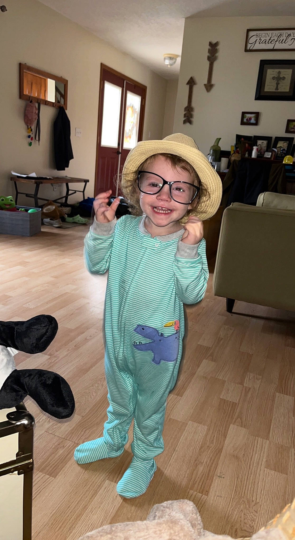 Kinsley is registered to the contest to win money with this photo: cap, couch, event, eyewear, floor, flooring, fun, glasses, happy, hardwood, hat, joint, joy, person, picture_frame, shoulder, smile, standing, sun_hat, toddler