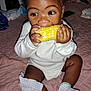 baby, child, corn_on_the_cob, eating, bedspread, quilt, socks, white_clothing, hands, face, curly_hair, indoor, cute, infant, munching, mischievous, young_child, portrait, sitting, food