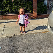 Celeste joined the competition — help win amazing prizes! toddler, child, sidewalk, stuffed_toy, pink, backpack, smile, sunlight, outdoor, concrete, fence, greenery, brick_wall, shoes, shorts, white_shirt, happy, person, shadow, urban