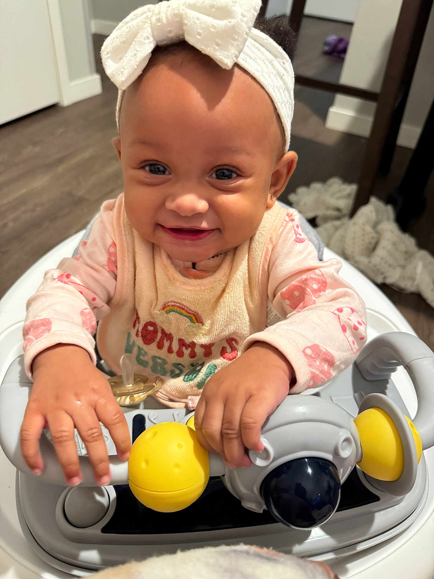 Delilah is registered to the contest to win money with this photo: baby, child, smiling, headband, bow, bib, toy, walker, hands, face, indoor, floor, blanket, clothing, person, happy, cute, infant, home, playtime