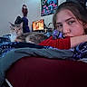 cat, person, face, bed, blanket, bedroom, indoors, portrait, relaxed, resting, sleepy, home, bedding, comforter, patterned_fabric, computer, artwork, wall, red_shirt, long_hair