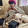 person, cat, dog, pets, couch, indoors, sitting, smartphone, bonnet, glasses, hoodie, animal_companions, sleepy, relaxed, portrait, living_room, window, cushion, blanket, playful