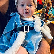 Dahlia is registered to the contest to win money with this photo: adult_hand, baby, beard, blue_outfit, bottle, child, cozy, curly_hair, cute, face, fur_trim, holiday_theme, indoor, lamp, nutcracker, portrait, smiling, table, tattoo, velvet