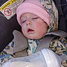 Dahlia is registered to the contest to win money with this photo: baby, bottle, car_seat, child, closeup, clothing, cute, face, floral_clothing, headwear, indoors, infant, peaceful, pink_hat, portrait, resting, safety, seatbelt, sleeping, warning_label