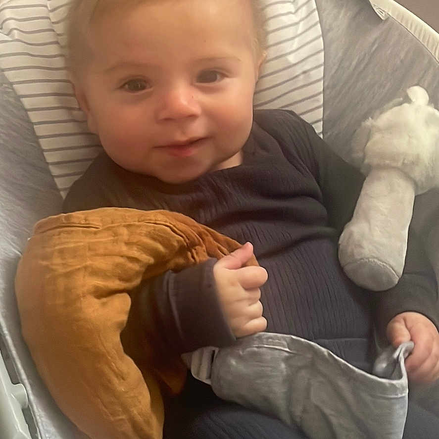 Albi joined the competition — help win amazing prizes! baby, baby_seat, black_clothing, child, comfortable, cozy, cute, feet, hand, indoor, infant, pillow, plush_toy, portrait, relaxed, seated, smiling, soft_lighting, striped_cushion, young_child