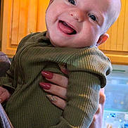 Arthur joined the competition — help win amazing prizes! baby, smiling, child, face, person, hand, nail_polish, long_nails, clothing, green_outfit, indoor, kitchen, cabinet, wood, countertop, dishwasher, bottle, happy, portrait, holding