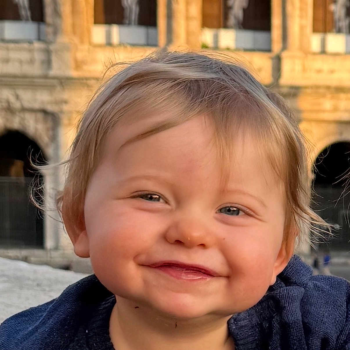 Eden a rejoint le concours — aidez-le/la à gagner de superbes lots ! toddler, child, smile, face, blue_eyes, blond_hair, sweater, portrait, outdoor, historic_building, stone_arch, sunlight, golden_hour, happy, cute, closeup, person, young_child, expression, warm_light