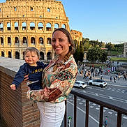 Eden a rejoint le concours — aidez-le/la à gagner de superbes lots ! woman, toddler, child, smile, colosseum, ancient_architecture, outdoor, daylight, cityscape, tourist, railing, street, people, car, tree, sky, clothing, braid, holding, travel