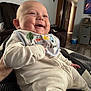 Jace is registered to the contest to win money with this photo: baby, smiling, laughing, infant, onesie, bib, indoor, living_room, furniture, blanket, cozy, person, child, happy, closeup, cute, head, face, human, toddler