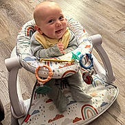 Jace is registered to the contest to win money with this photo: baby, infant, smiling, baby_seat, toy, pacifier, floor, wooden_floor, rainbow_pattern, clothing, bib, happy, cute, indoor, child, person, seat, play, footwear, baby_toys