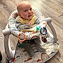 baby, infant, smiling, baby_seat, toy, pacifier, floor, wooden_floor, rainbow_pattern, clothing, bib, happy, cute, indoor, child, person, seat, play, footwear, baby_toys