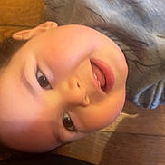 Yusuf a rejoint le concours — aidez-le/la à gagner de superbes lots ! child, toddler, baby, face, close_up, smile, eyes, mouth, tongue, cheeks, hair, indoor, wood_floor, floor, shirt, candid, playful, happy, portrait, casual_clothing