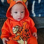 baby, child, orange_onesie, tigger, hooded_clothing, sitting, couch, blanket, indoor, cute, face, eyes, hands, infant, portrait, warm_clothing, toddler, cozy, soft_fabric, clothing
