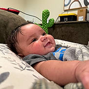 Kamari joined the competition — help win amazing prizes! baby, infant, smiling, face, cheeks, arm, pillow, blanket, cactus_plush, couch, indoor, curly_hair, clothing, pattern, soft_light, close_up, happy, child, person, home