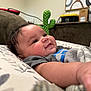 baby, infant, smiling, face, cheeks, arm, pillow, blanket, cactus_plush, couch, indoor, curly_hair, clothing, pattern, soft_light, close_up, happy, child, person, home