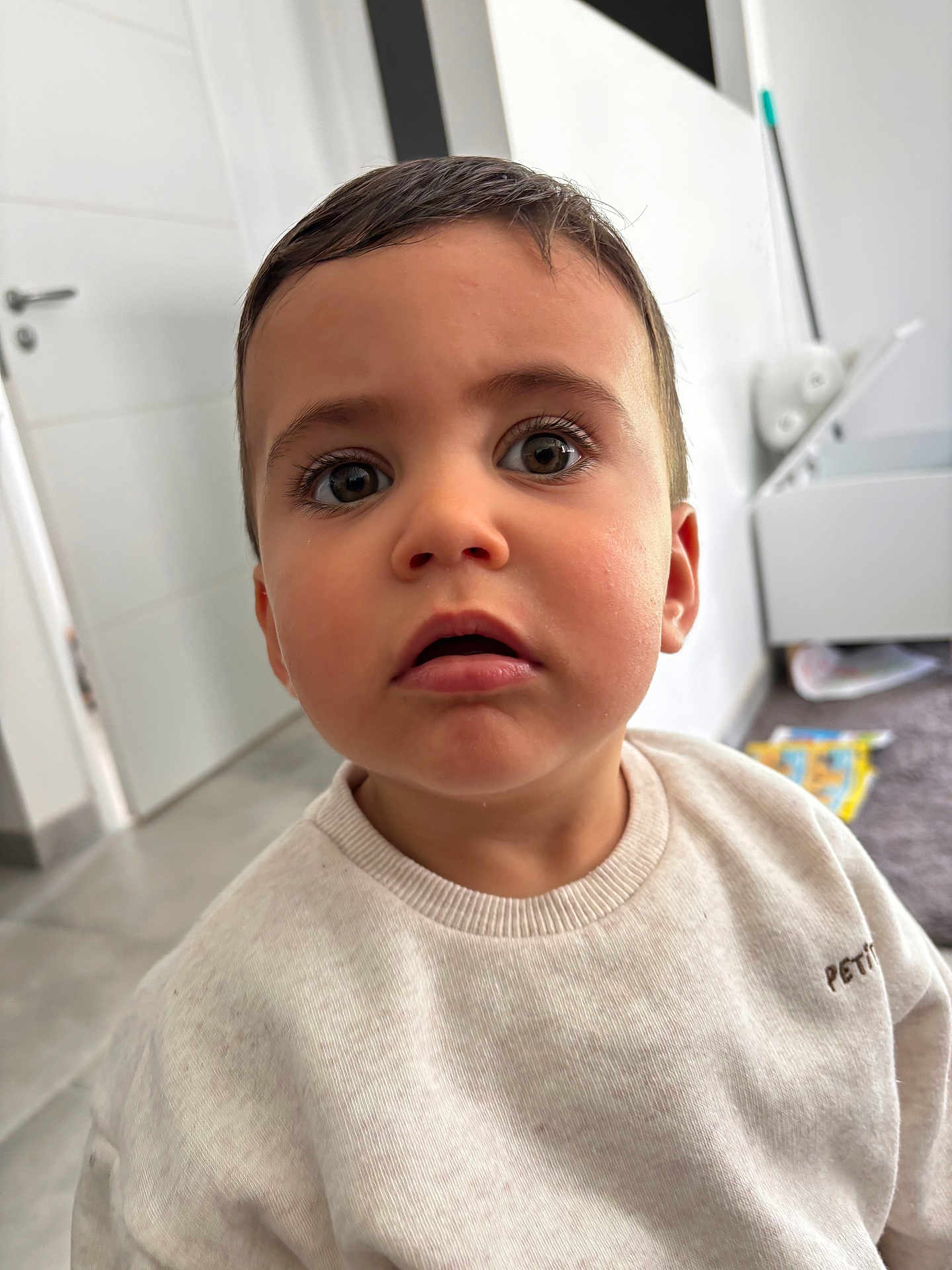Marius participe au concours pour gagner de l'argent avec cette photo : toddler, child, face, indoor, sweater, curious, eyes, mouth, expression, person, young, portrait, clothing, room, door, floor, blurry_background, casual, cute, skin