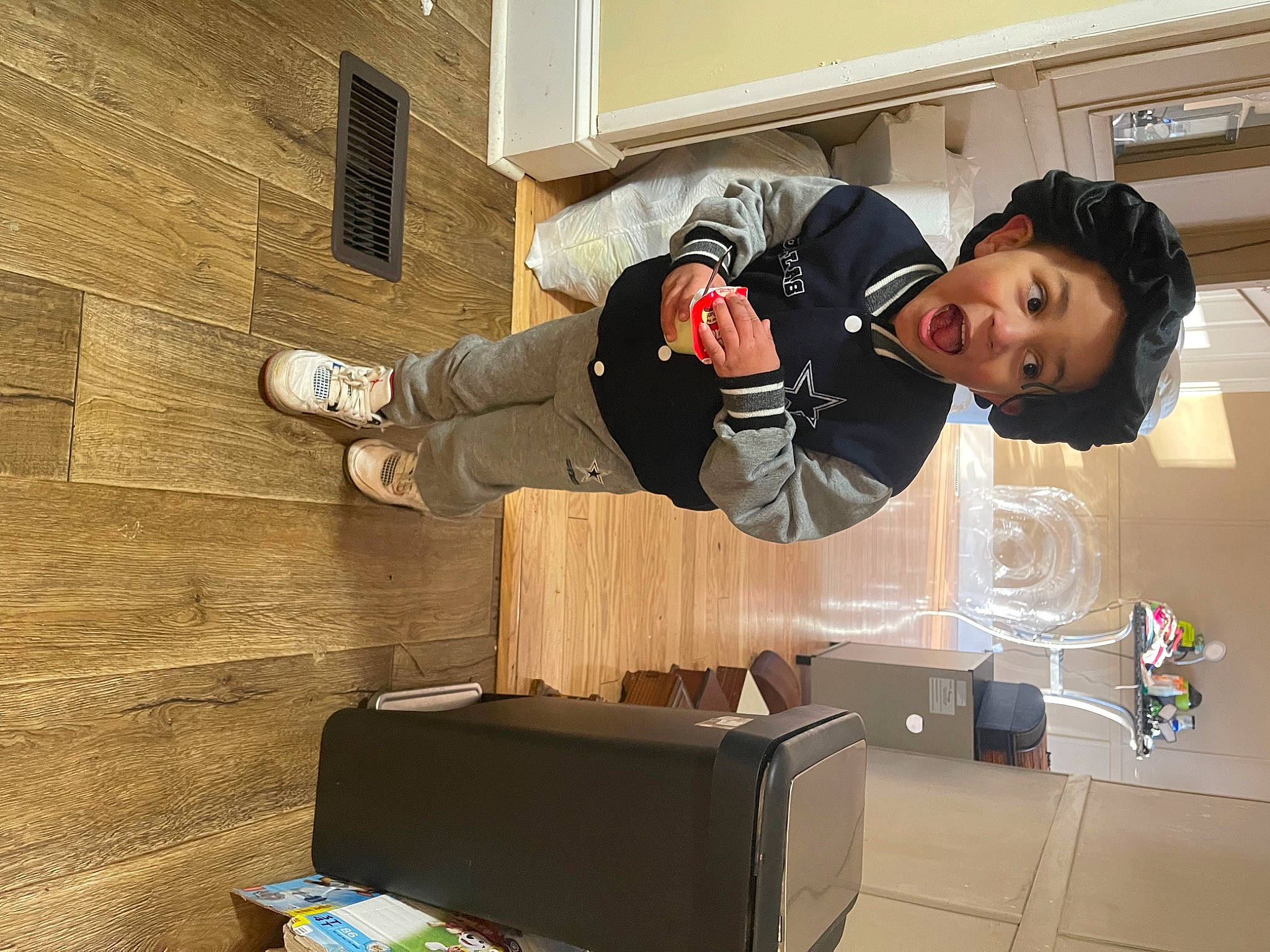 Grayson is registered to the contest to win money with this photo: audio_equipment, cardboard, carton, flooring, fun, hardwood, jacket, person, room, shipping_box, sitting, surprise, window, wood