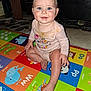 baby, child, blue_eyes, onesie, play_mat, colorful, animal_print, indoor, floor, smile, sitting, cute, infant, person, childhood, stains, hand, foot, face, bright