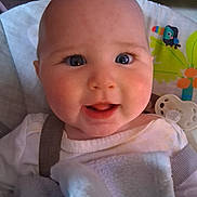 Chloe is registered to the contest to win money with this photo: baby, infant, face, blue_eyes, smile, blanket, white_clothing, pacifier, close_up, cheeks, cute, indoors, child, happy, person, seatbelt, colorful_background, toy, head, portrait