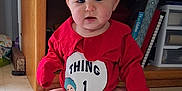 Chloe joined the competition — help win amazing prizes! baby, child, red_clothing, thing_1, floor, sitting, indoors, blue_eyes, curious, wooden_shelf, books, storage_drawers, barefoot, tiled_floor, infant, cute, person, face, home, casual