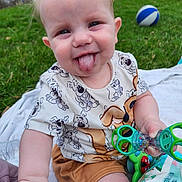 Cristian is registered to the contest to win money with this photo: baby, child, tongue_out, playful, grass, outdoor, toy, ball, blanket, smiling, cute, toddler, clothing, shorts, shirt, hand, face, happy, fun, nature