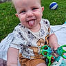 baby, child, tongue_out, playful, grass, outdoor, toy, ball, blanket, smiling, cute, toddler, clothing, shorts, shirt, hand, face, happy, fun, nature
