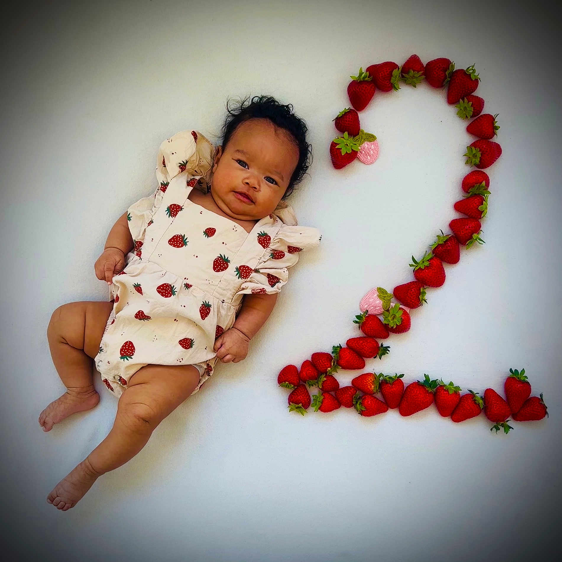 Isabella is registered to the contest to win money with this photo: baby, celebration, child, cute, fresh_fruit, fruit, green, healthy, infant, laying_down, milestone, natural, number_two, patterned_clothing, portrait, red, skin, strawberry, summer, white_background