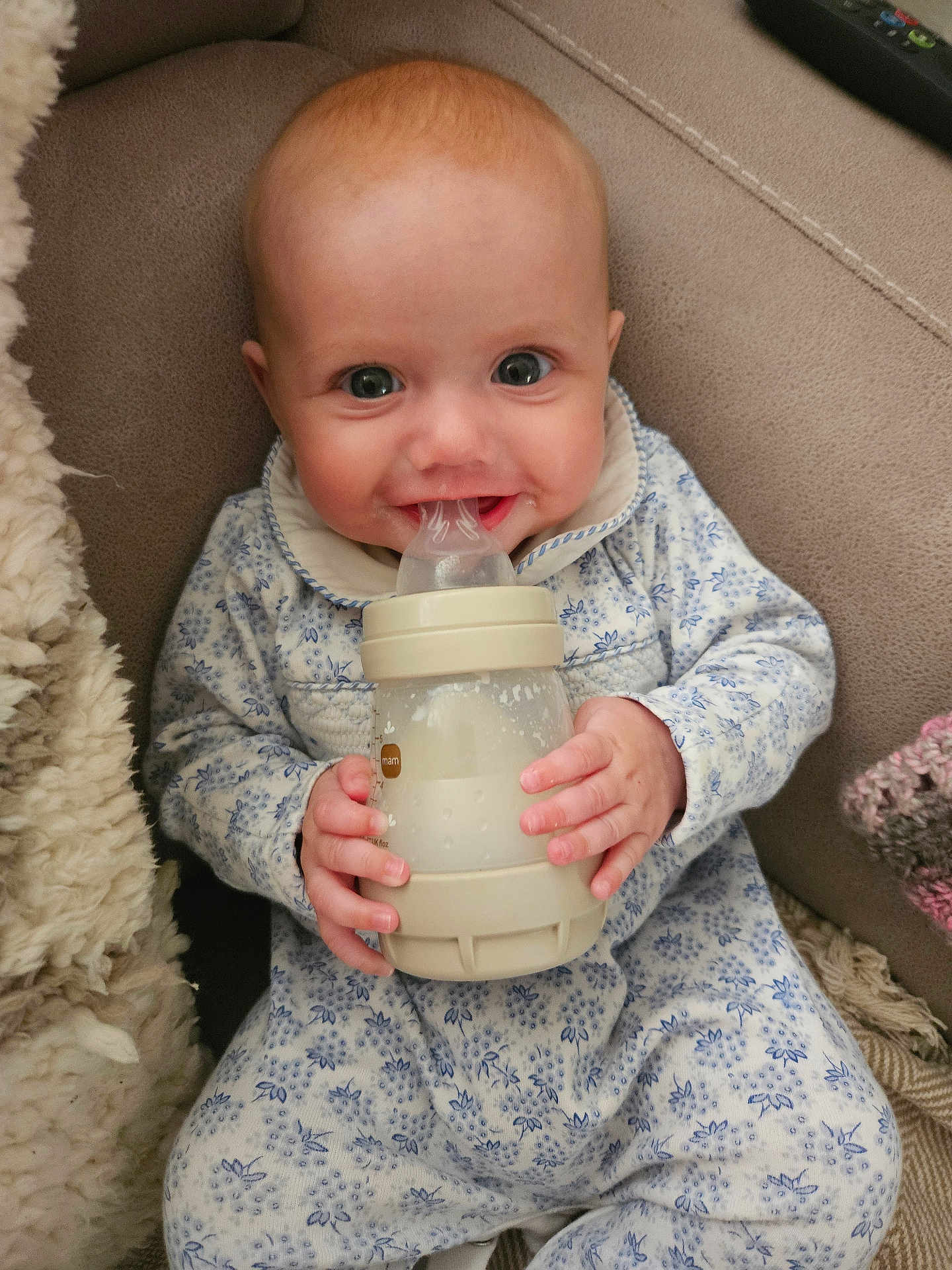 Aria is registered to the contest to win money with this photo: baby, infant, bottle, milk, cute, smiling, blue, onesie, clothing, sitting, blanket, couch, soft, hand, face, expression, child, indoors, portrait, happy