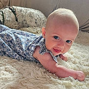 Aria is registered to the contest to win money with this photo: baby, infant, smiling, blue_flower_dress, fluffy_rug, dog, curly_fur, couch, indoor, cute, tongue_out, person, pet, resting, cozy, happy, portrait, child, home, toddler