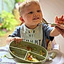 Cobie is registered to the contest to win money with this photo: toddler, child, baby, high_chair, bib, food, plate, spoon, meal, smiling, indoor, feeding, happy, person, cute, blond_hair, table, hand, kitchen, domestic