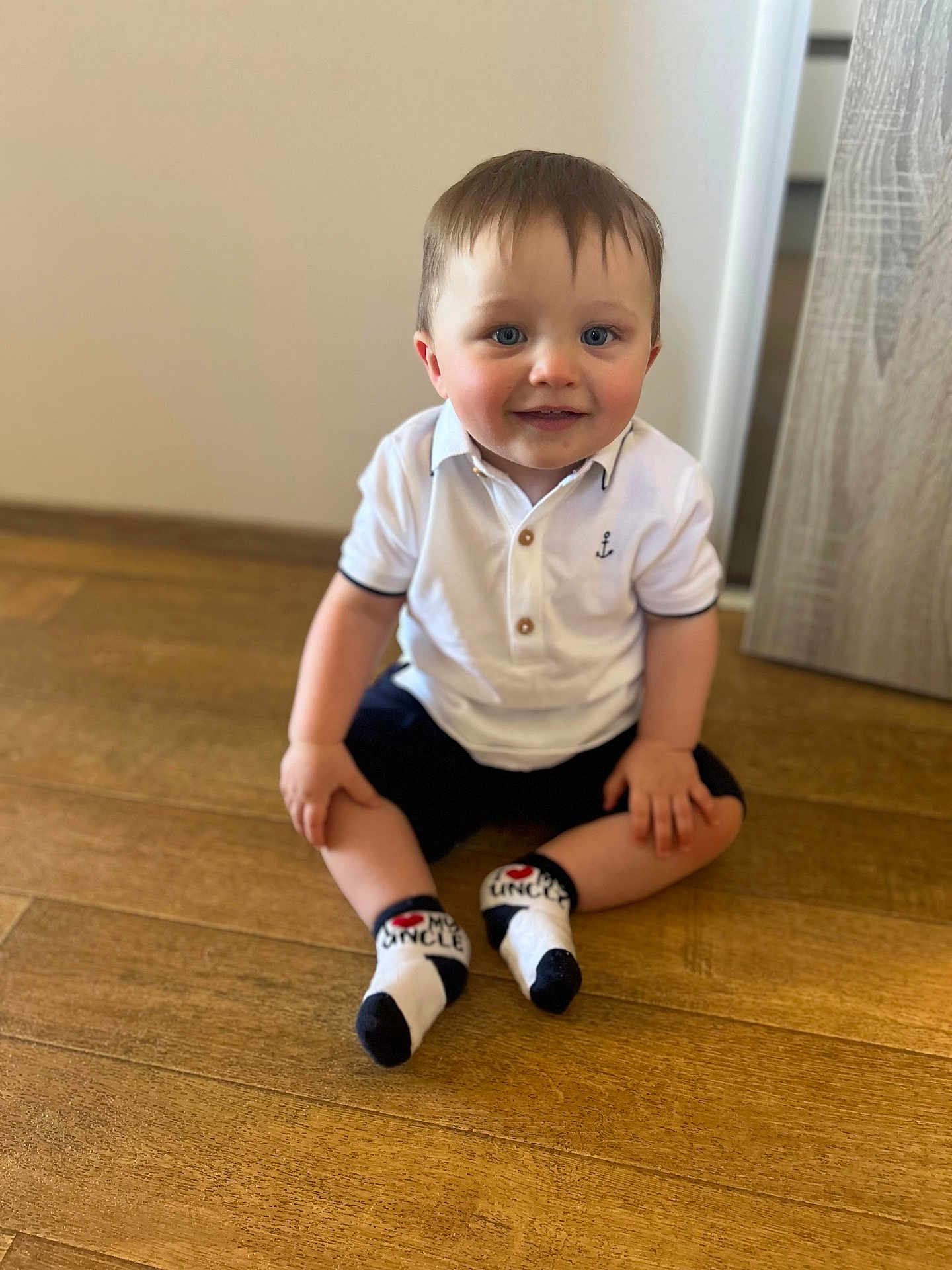 Cobie is registered to the contest to win money with this photo: toddler, child, boy, sitting, floor, white_polo_shirt, socks, blue_eyes, wooden_floor, indoor, cute, smiling, short_hair, casual_clothing, happy, person, baby, portrait, young_child, home