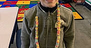 Koltyn is registered to the contest to win money with this photo: boy, candy_necklace, child, classroom, clothing, colorful, concrete_floor, educational_rug, eyes, face, hair, indoor, learning_environment, person, shelves, smiling, standing, table, young, zipper_jacket
