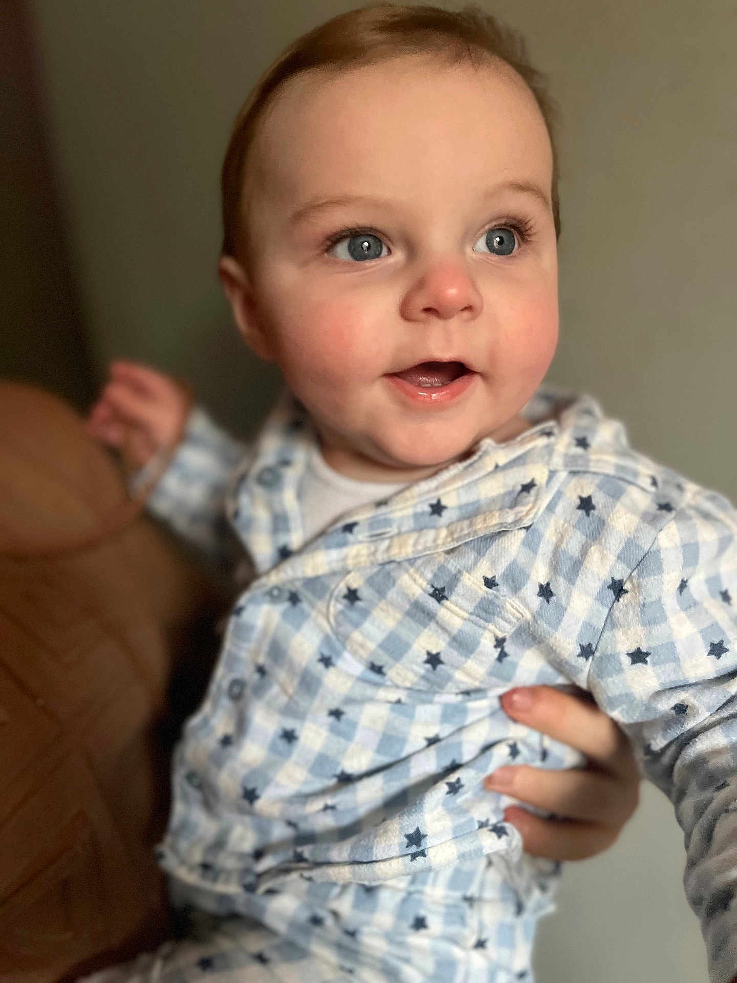 Paul is registered to the contest to win money with this photo: baby, child, face, blue_eyes, rosy_cheeks, clothing, pattern, stars, hand, adult, holding, portrait, indoor, cute, smiling, closeup, soft_light, warm, expression, infant