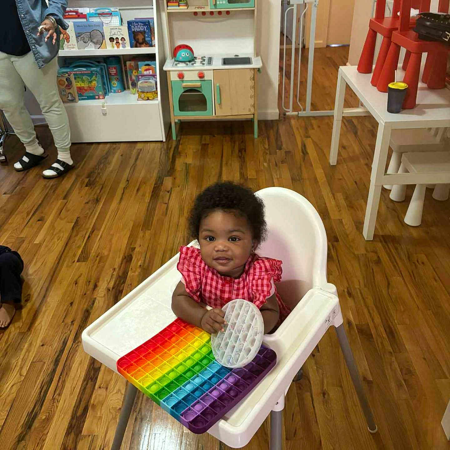 Zamora joined the competition — help win amazing prizes! adult, baby, bookshelf, child, childrens_books, colorful, furniture, high_chair, home, indoor, person, plastic_chair, play, pop_it_toy, red_chair, room, smiling, toys, wood_floor, wooden_floor