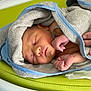 newborn, baby, sleeping, towel, hand, skin, infant, resting, closeup, soft_texture, blue_trim, green_background, peaceful, cute, wrapped, person, human, tiny, portrait, fresh