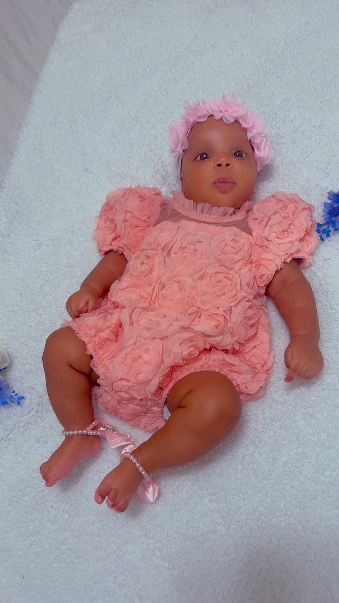 Brianna is registered to the contest to win money with this photo: baby, infant, pink_dress, flower_headband, pearls, anklets, soft_surface, white_background, cute, lying_down, curious_expression, child, newborn, adorable, portrait, skin, baby_fashion, decorative_clothing, footwear_accessories, close_up