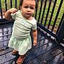 toddler, child, outdoor, porch, wooden_floor, rain, wet_surface, curly_hair, topknot, green_dress, brown_boots, expression, serious_face, grass, railing, tree_trunk, nature, daylight, person, standing