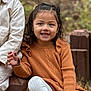 casual_clothing, child, curly_hair, cute, daylight, face, fall, fun, happy, nature, orange_sweater, outdoor, person, portrait, sitting, smiling, striped_pants, warm_colors, wooden_steps, young_child