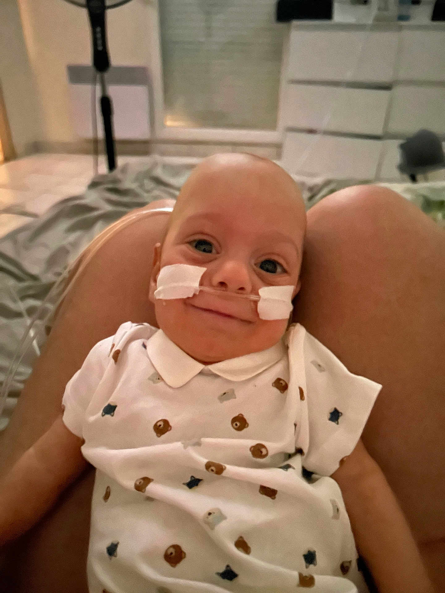 Maël participe au concours pour gagner de l'argent avec cette photo : baby, infant, nasal_cannula, smile, white_shirt, bear_pattern, star_pattern, legs, indoor, bed, blanket, medical, healthcare, person, human, child, cute, portrait, comfort, cozy
