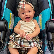 Alexis joined the competition — help win amazing prizes! baby, child, car_seat, plaid, headband, skirt, smile, happy, toenails, painted_nails, clothing, infant, seatbelt, indoor, person, young_child, cheerful, cute, fashion, sitting