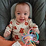baby, smiling, toy, cushion, clothing, face, infant, happy, cute, child, indoor, sitting, colorful, play, comfort, person, seat, expression, hand, wearing