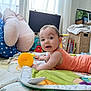 baby, child, infant, play_mat, toy, orange_onesie, cushion, indoor, curious, face, expression, furniture, books, blanket, window, daylight, floor, room, smiling, cute