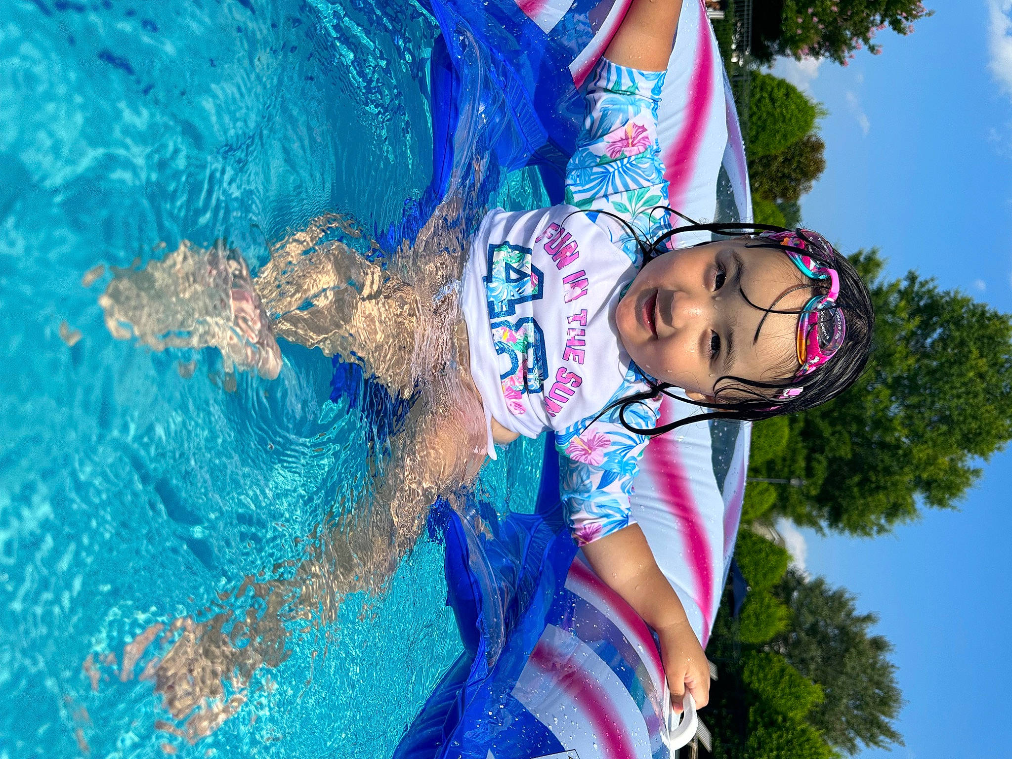 Arabella is registered to the contest to win money with this photo: azure, black_hair, child, cool, electric_blue, eyewear, facial_expression, fun, grass, happy, headwear, leisure, people_in_nature, person, plant, recreation, sky, swimming_pool, swimwear, tree