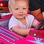 amusement_ride, blue_eyes, bright_colors, carnival, child, face, fun, hand, indoor, person, pink, playful, ride, seat, short_hair, smiling, steering_wheel, toddler, toy_car, white_shirt