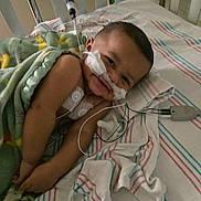 Veylin is registered to the contest to win money with this photo: baby, hospital, crib, medical_tubes, blanket, smile, face, child, monitoring_wires, striped_sheet, healthcare, lying_down, cute, infant, toddler, medical_equipment, cozy, child_patient, happy, hospital_bed