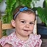 toddler, child, smiling, headband, blue_bow, pink_dress, patterned_clothing, wooden_chair, green_plants, indoor, portrait, cute, happy, face, person, baby, short_hair, candid, seated, natural_light