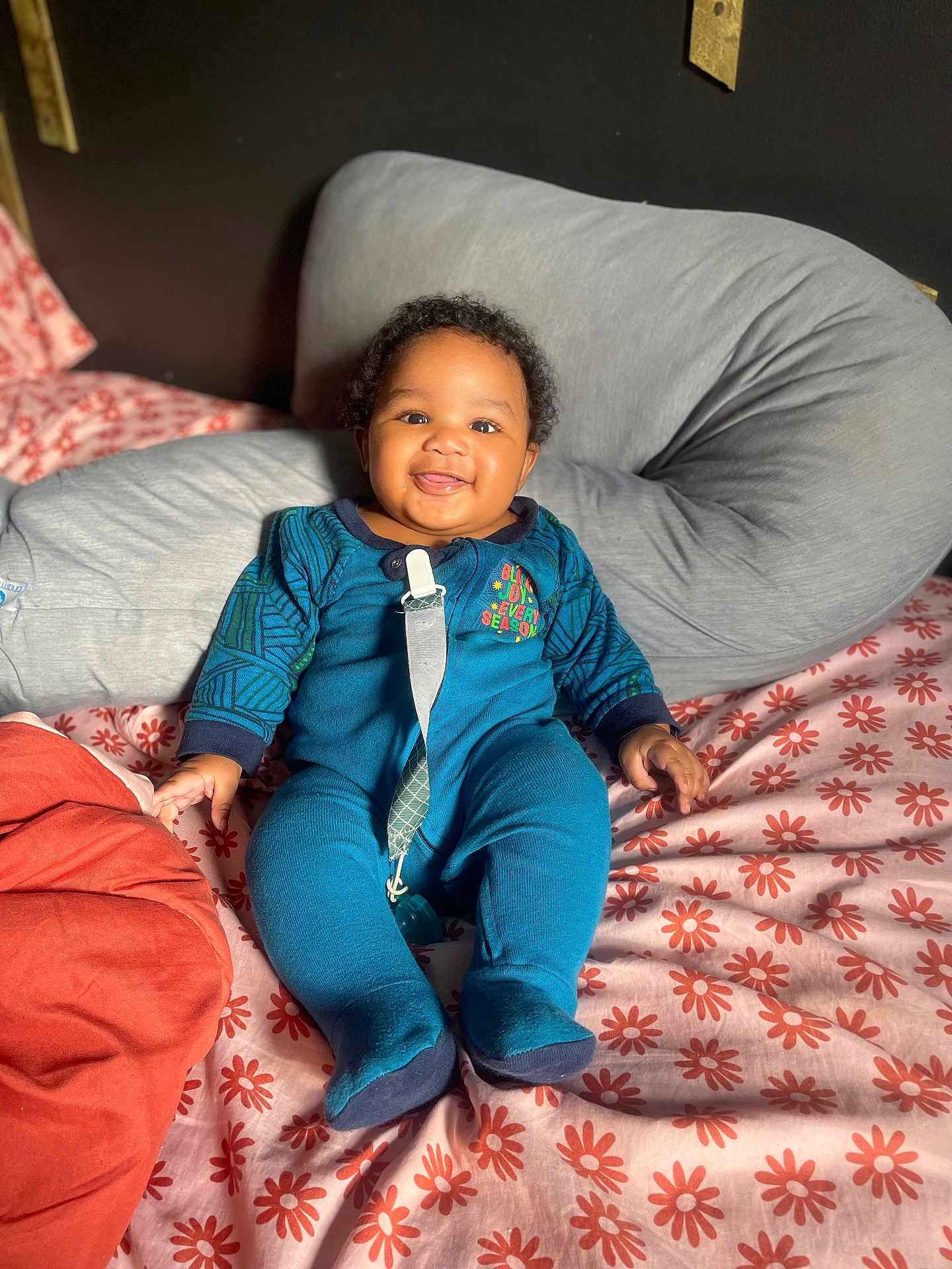Kyzeir Walker joined the competition — help win amazing prizes! baby, smiling, blue_onesie, bed, pillow, floral_pattern, indoors, child, cute, happy, person, infant, face, sitting, blanket, soft_fabric, pacifier_clip, cozy, portrait, curly_hair